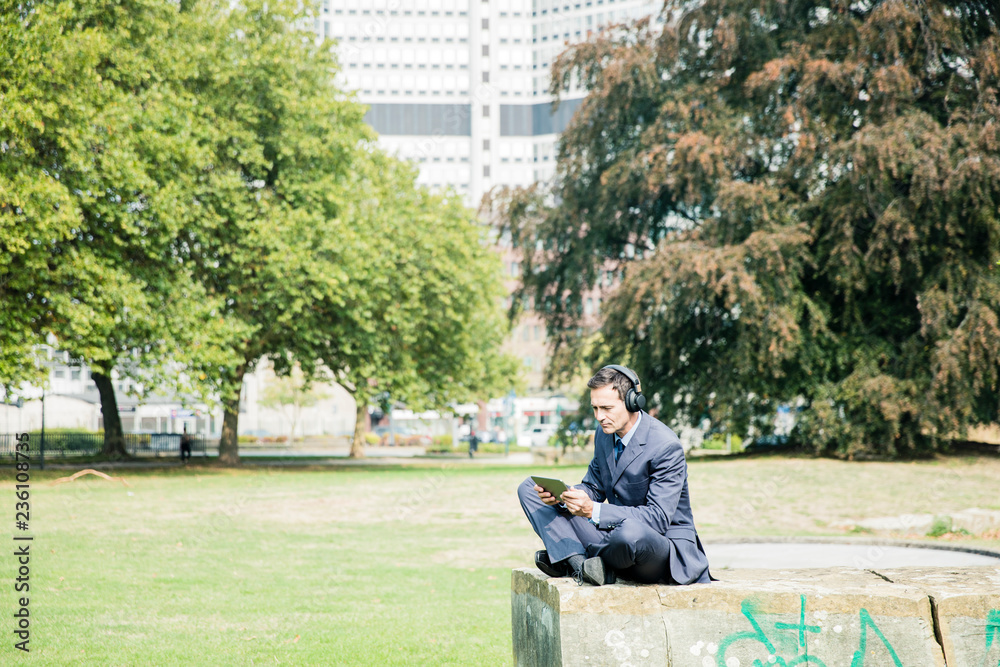 Businessman in city park wearing headphones and using tablet Businessman in city park wearing headphones and using tablet