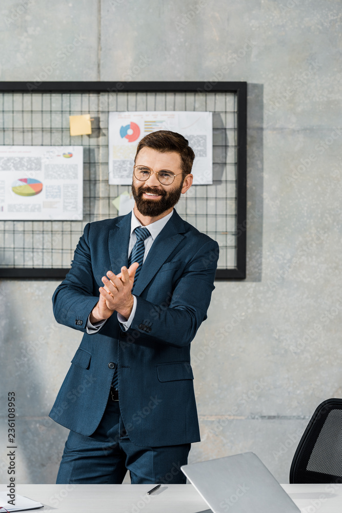 happy bearded businessman applauding and smiling at camera in office happy bearded businessman applauding and smiling at camera in office