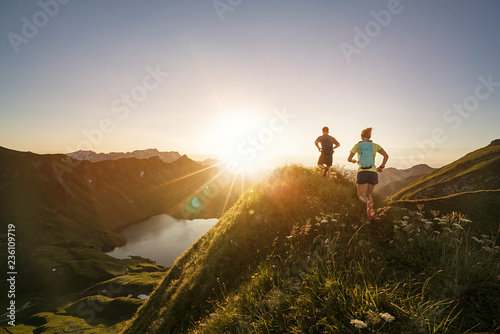 Man and woman running on mountain trail during sunrise photo
