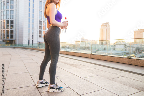 Sexy sports girl in the sunset. Sports girl with beautiful legs in leggings and a bottle of water in her hands.Girl with a beautiful bottom doing sports on the background of a beautiful city landscape photo