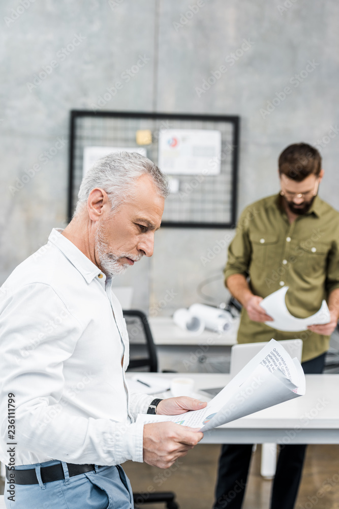 handsome businessmen looking at blueprints in office handsome businessmen looking at blueprints in office