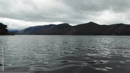 Aerial, drone shot, close to the water, towards a white sail boat, in the distance, sailing in the dark water, of Derwentwate lake, on a cloudy and gloomy day, in Kerswick, England, United kingdom photo