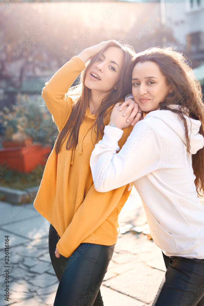 two young girls walking city having fun. joyful Women in bright colored hoodies walking, laughing and posing on the street