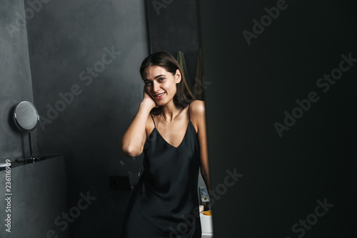 Smiling young woman standing at the mirror at the bathroom