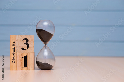 December 31st set on wooden calendar and hourglass with blue background.
