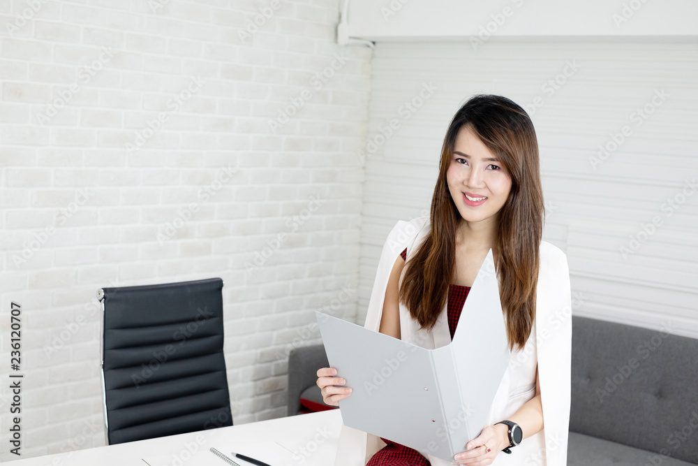 Portrait of beautiful Asian business woman sitting on the table and holding the opened folder Portrait of beautiful Asian business woman sitting on the table and holding the opened folder