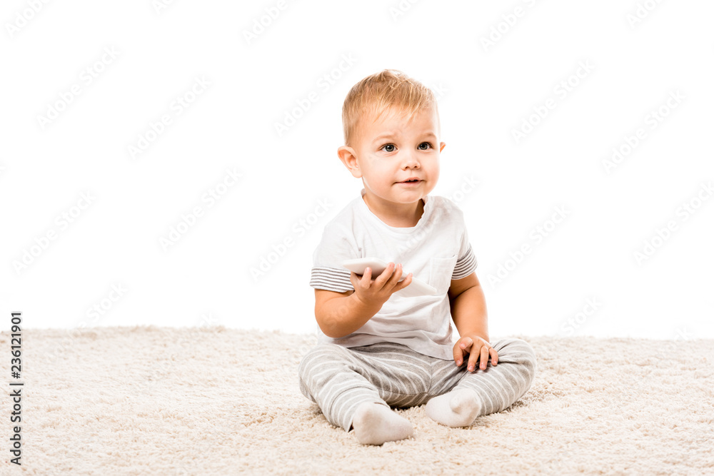 adorable toddler boy with smartphone sitting on carpet isolated on white adorable toddler boy with smartphone sitting on carpet isolated on white