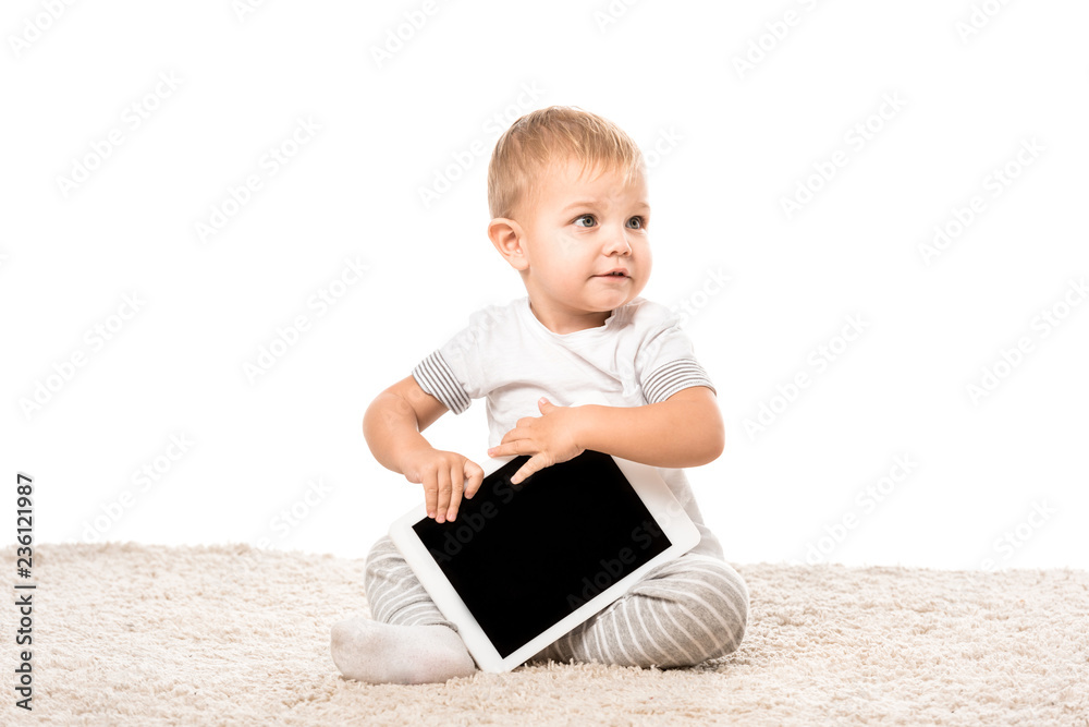 nice toddler boy sitting on carpet and holding digital tablet isolated on white nice toddler boy sitting on carpet and holding digital tablet isolated on white