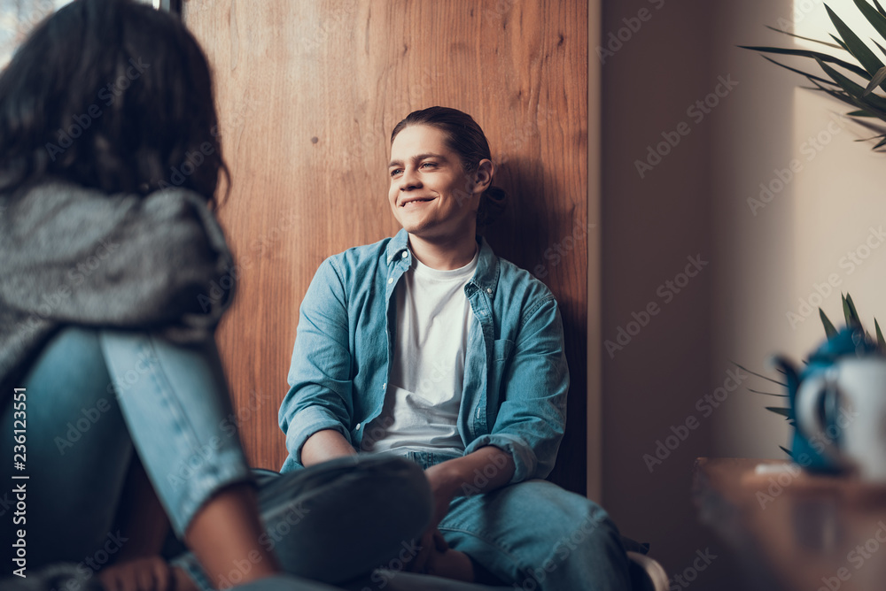 Relaxed handsome man in casual clothes feeling good and smiling while having pleasant meeting and sitting on the window sill with his girlfriend