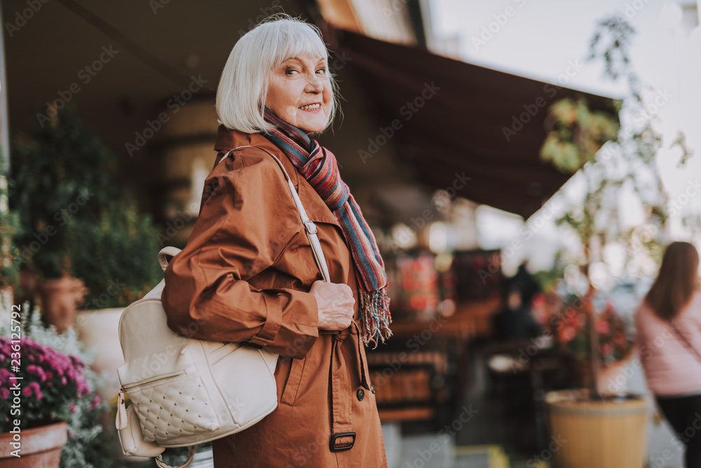 Time for a walk. Waist up portrait of old woman in coat looking at camera and smiling