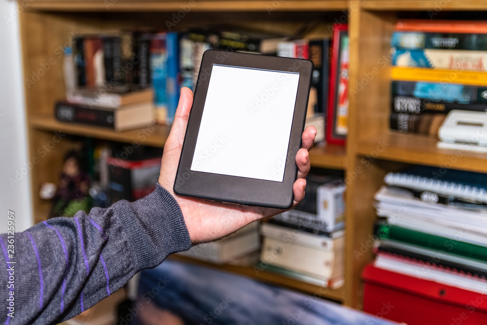 Male hands holding digital reading device in front of bookshelves stock