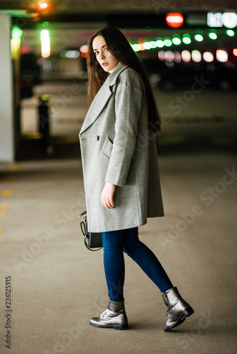Beautiful young girl in a gray coat and with bag on car parking