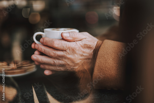 : Enjoying favorite beverage. Close up of senior man hands with white cup of cappuccino