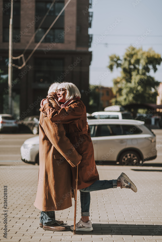 Side view full length portrait of stylish old lady embracing husband while standing on the street