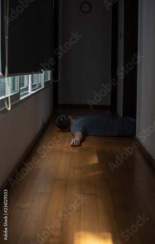 An old man lying down unconscious from a sudden heart attack in front of his bed room in a modern house during COVIT era. He left alone on the wooden floor on the walkway.