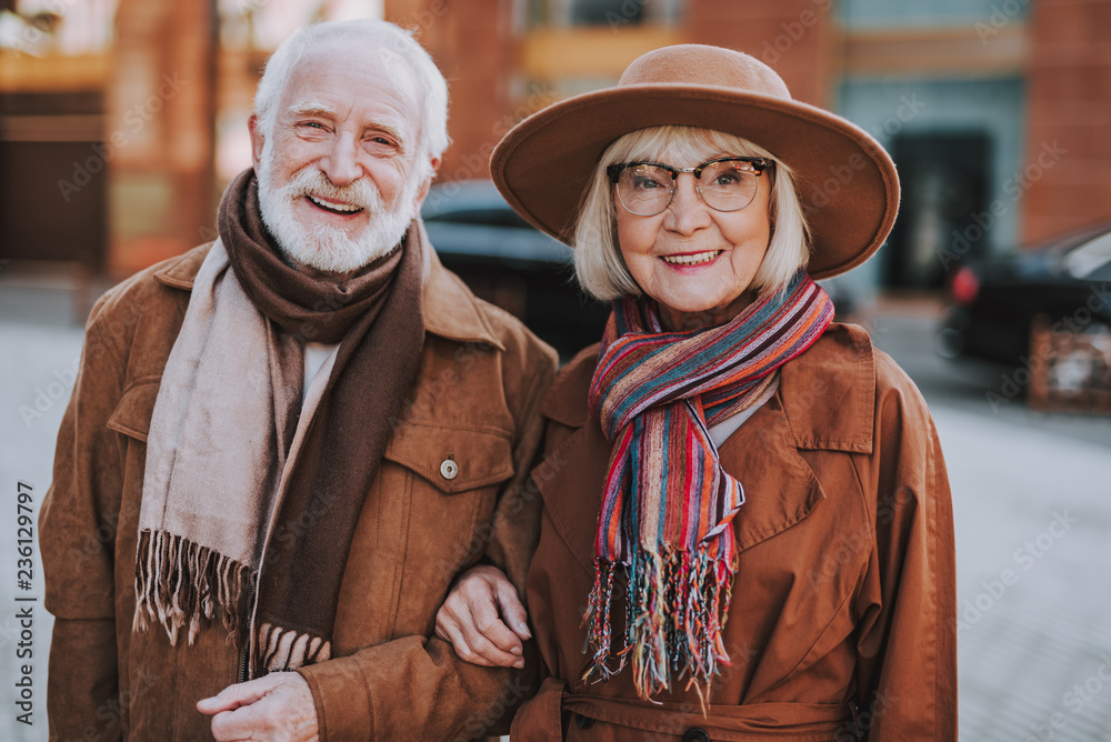 Happy together. Waist up portrait of elderly bearded man spending time with his wife outdoors. They looking at camera and smiling