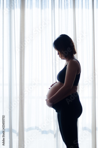 woman pregnant standing near curtain, shot in a dark tone