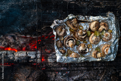 Baked mushrooms in foil on grill on coals. Lunch tourist in forest