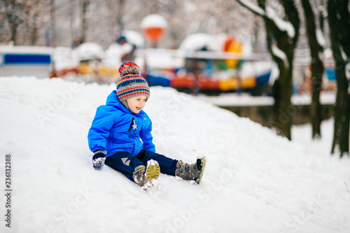 Child sitting on snowy mountain. Winter children's fun