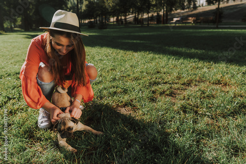Cheerful lady in hat is playing with her pet while spending time in park. Copy space on right side
