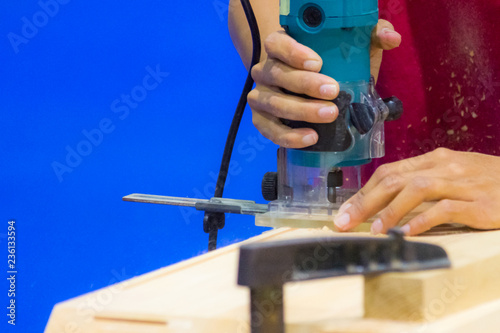 Carpenter working with electric planer on wooden plank in workshop