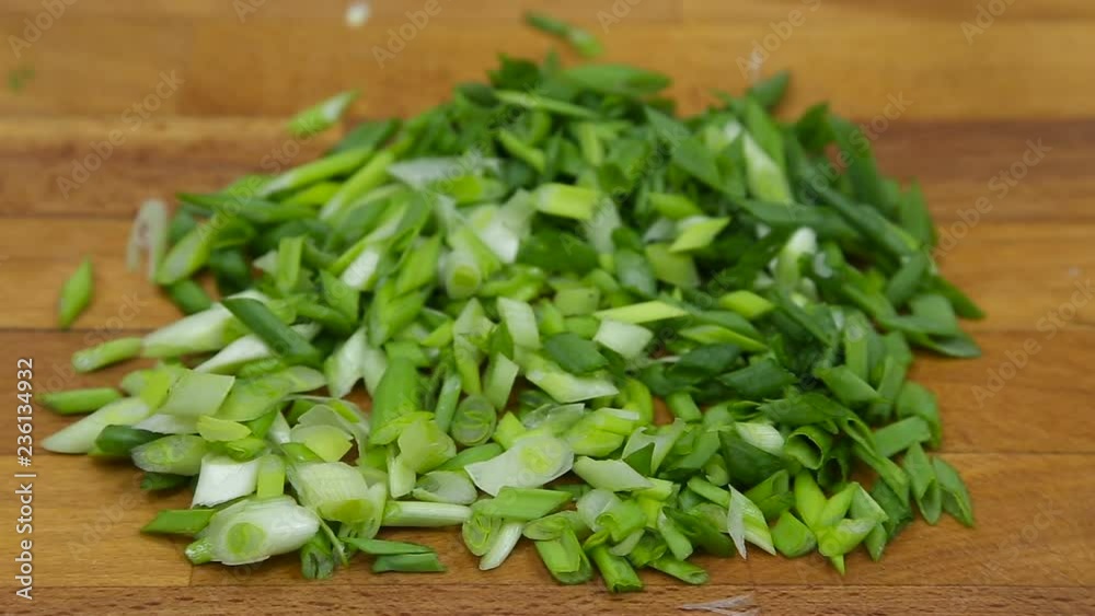 A pile of chopped green onion on wooden cutting board with black background A pile of chopped green onion on wooden cutting board with black background