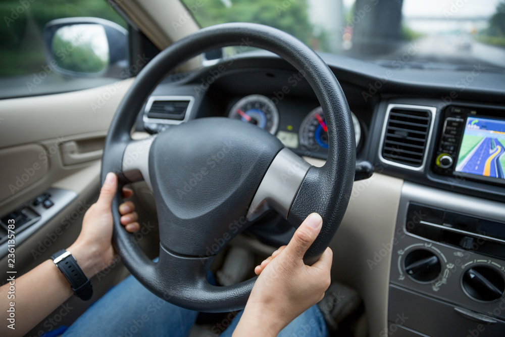 Hands holding steering wheel while driving car on city road Hands holding steering wheel while driving car on city road