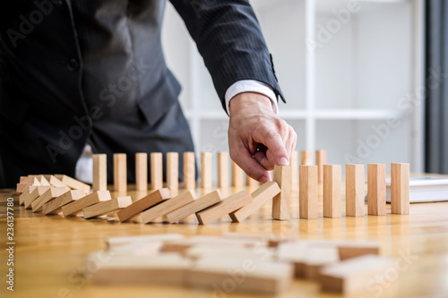Wooden game strategy, Businessman hand stopping falling wooden dominoes effect from continuous toppled or risk, strategy and successful intervention concept for business