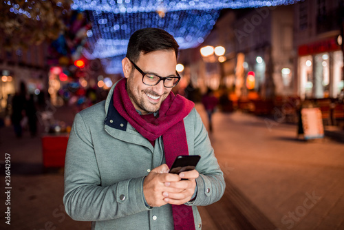 Portrait of a young man using smartphone on the street with Christmas decoration.