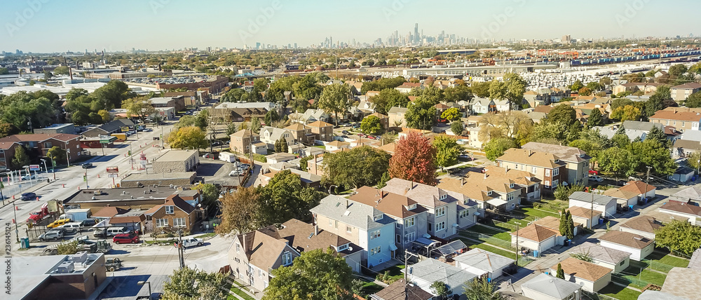 Naklejka premium Panorama widok z lotu ptaka tradycyjnej dzielnicy mieszkalnej na zachód od Chicago. Rząd klasycznego domu z ogrodem i garażem wolnostojącym. Linie horyzontu od śródmieścia w tle