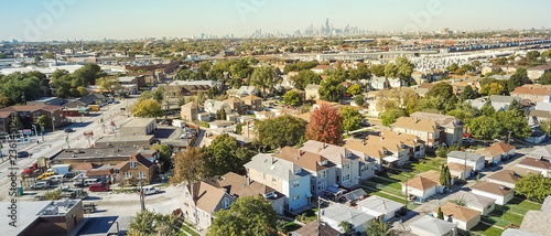 Panorama aerial view traditional residential neighborhood west of Chicago. Row of classic house with garden and detached garage. Skylines from downtown in background