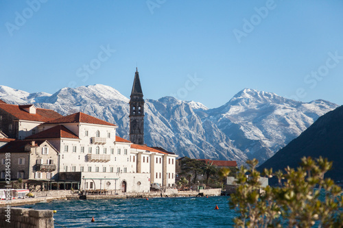 Winter in Montenegro. Perast in the Bay of Kotor with snow peaks of mountains, blue cold the Adriatic Sea, old town with ancient architecture, stone houses and tiled roofs.