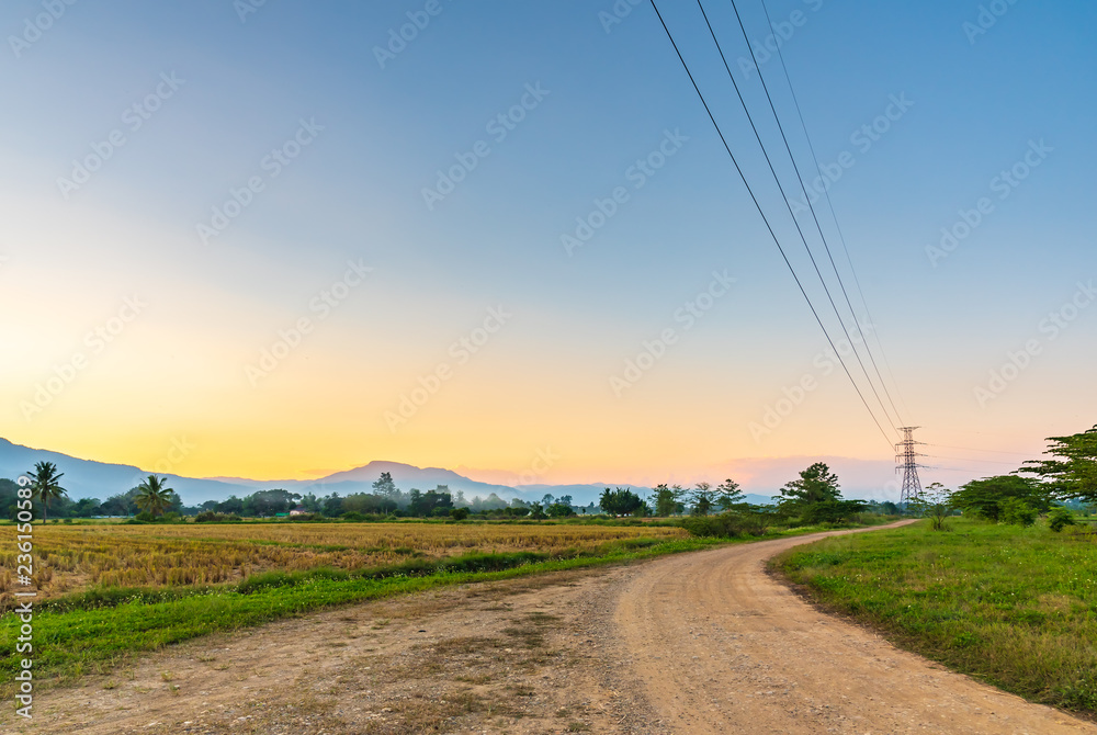 Dirt and gravel country road through rice field in countryside of Thailand.