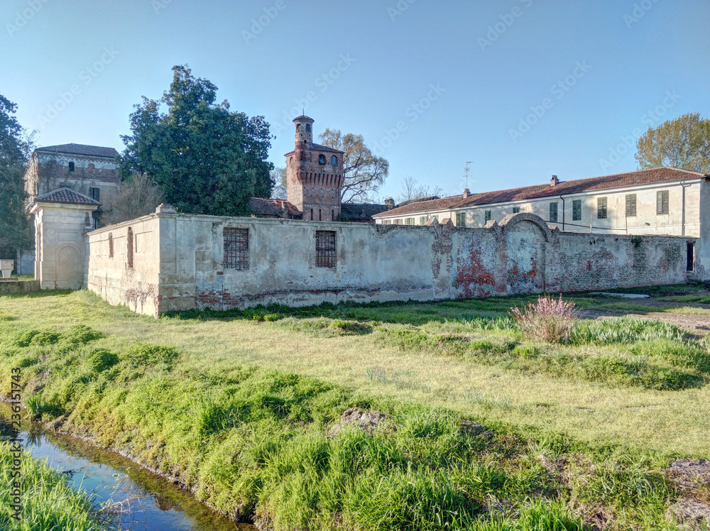 The old cotto bricks made abandoned castle of Albano Vercellese, Piedmont region, Italy, next to a green lawn and an artificial canal