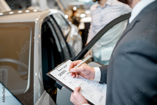 Manager filling car rental documents standing in the showroom with car on the background