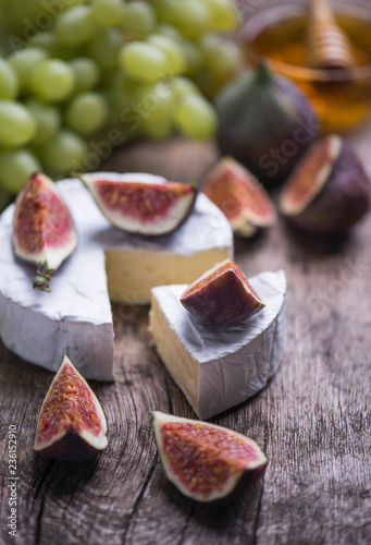 The set of natural products - soft cheese, figs, grape, honey on a wooden board.