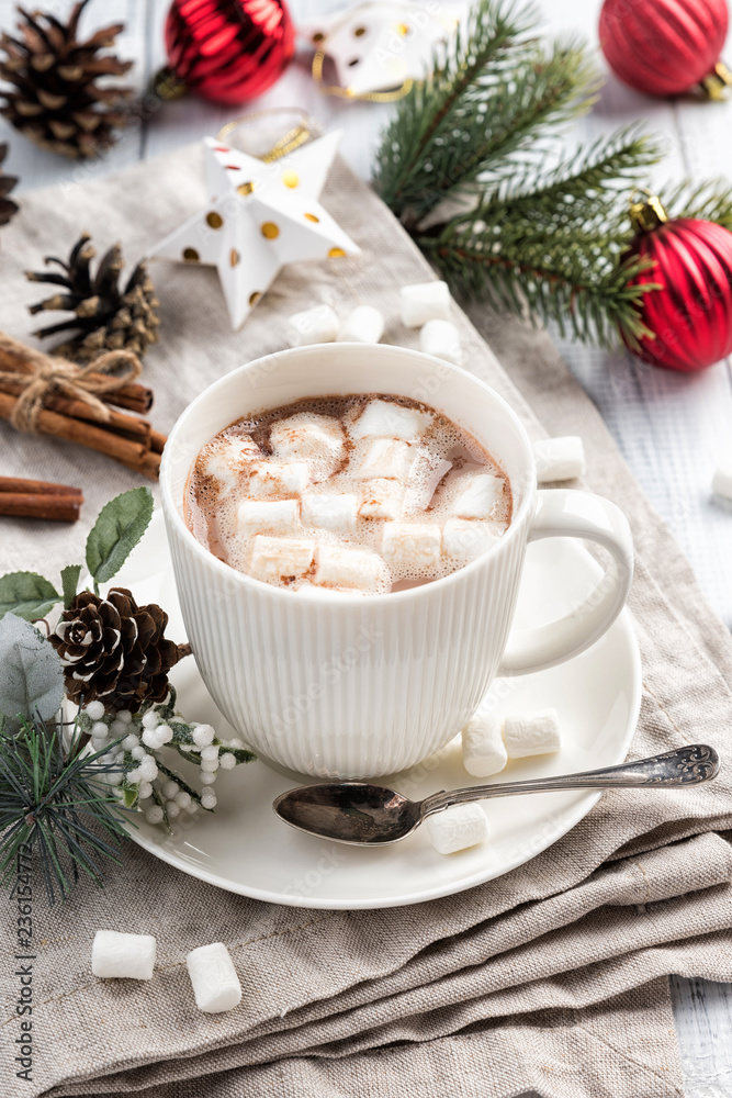 Cup of hot chocolate with marshmallow and cinnamon sticks on the white wooden table. Winter cocoa drink on a napkin, Christmas-tree golden stars and red balls decorations, branches and cones Cup of hot chocolate with marshmallow and cinnamon sticks on the white wooden table. Winter cocoa drink on a napkin, Christmas-tree golden stars and red balls decorations, branches and cones