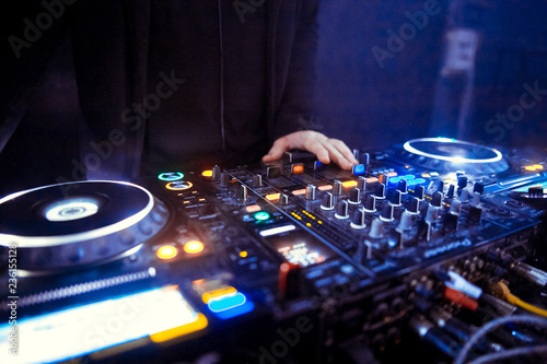Hands of a DJ mixing music at a disco or concert with one hand on the switches and one held near the vinyl record on the turntable