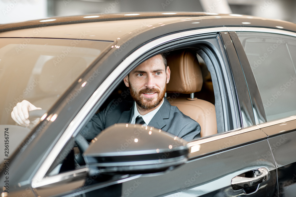 Portrait of an elegant businessman sitting on the driver seat in the luxury car at the showroom