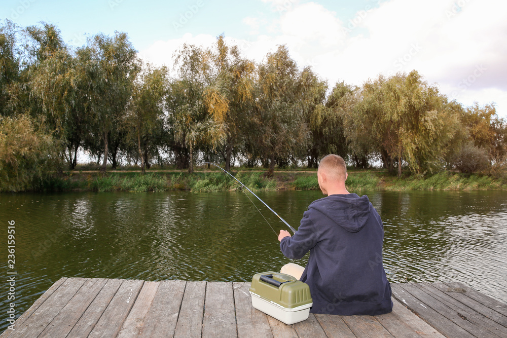 Man fishing on wooden pier at riverside. Recreational activity Man fishing on wooden pier at riverside. Recreational activity
