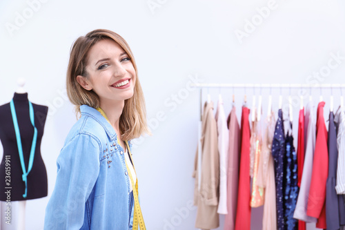 Beautiful young stylist at workplace near rack with clothes. Space for text