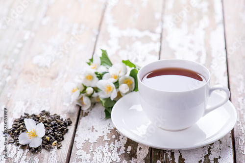 Green tea in a white cup with dry tea leaf and jasmine flowers on a wooden background with copy space.