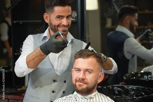 Barber doing trendy haircut to young man in barber shop