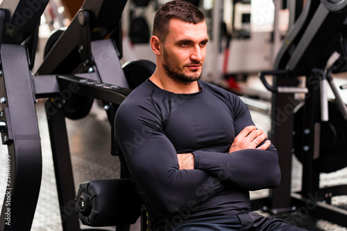 Young handsome fitness trainer sits modern gym