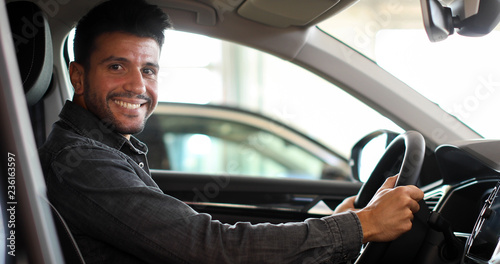 Young man smiling in his new car in a showroom © Minerva Studio