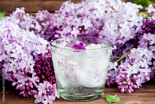 Fresh lilac flower petals floating on water in glass on a dark wooden background