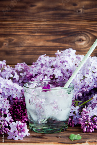 Fresh lilac flower petals floating on water in glass on a dark wooden background