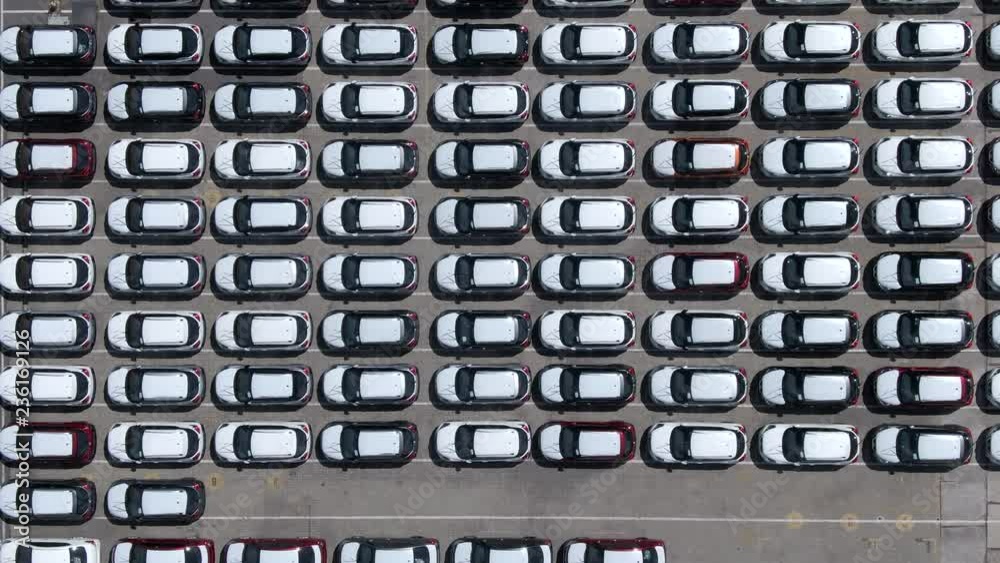 Aerial top down view of parking lot filled with brand new cars waiting for sale and transportation. Flying over large parking area at shipping docks, automobile industry. Aerial top down view of parking lot filled with brand new cars waiting for sale and transportation. Flying over large parking area at shipping docks, automobile industry.