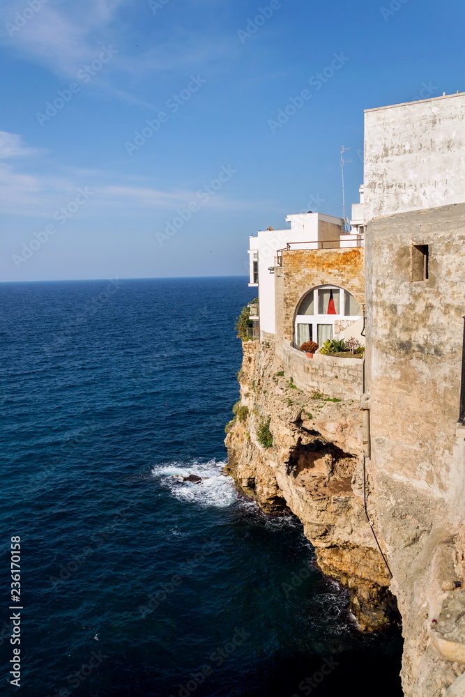 Traditional houses on dramatic cliffs with caves rising from Adriatic sea in Polignano a Mare, Italy, sunny summer day