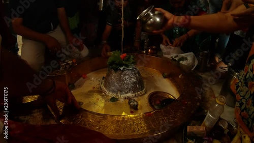 Hands of big crowd of people pour water and milk over swayambhu self-existing lingam and put leaves and flowers in ancient hindu temple Rishikesh
